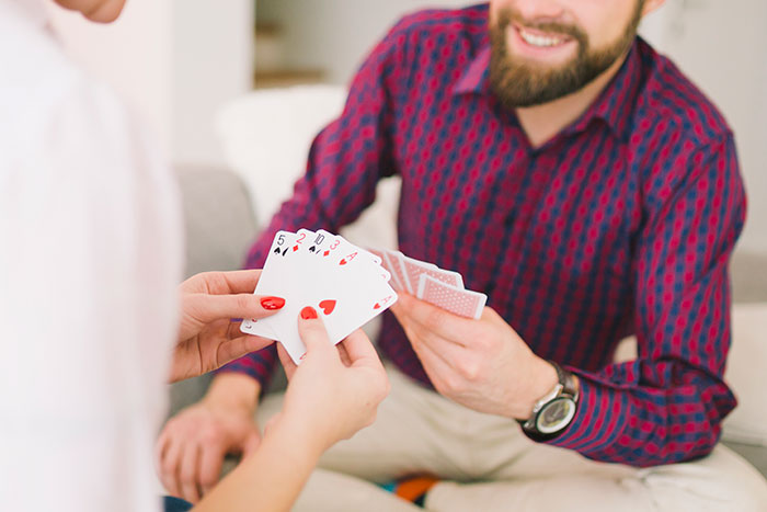 Couple playing cards on a date, smiling and holding hands of cards, capturing awkward moments during conversation.
