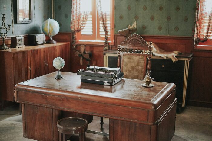 Vintage wooden desk with typewriter and globe in an old study room, evoking disturbing things found after a loved one’s death.