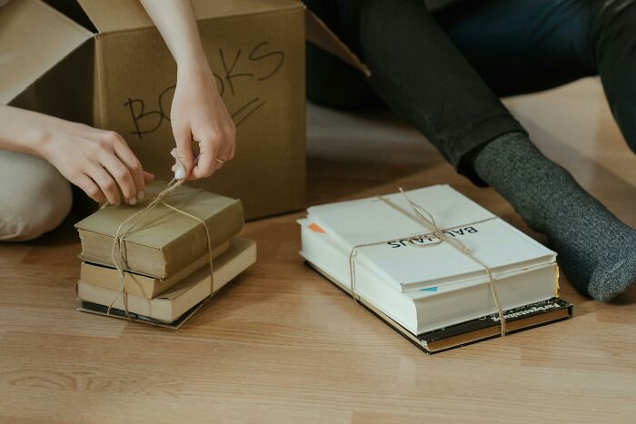 Person tying books with string near a box labeled books, illustrating surprising and disturbing finds after a loved one’s death.