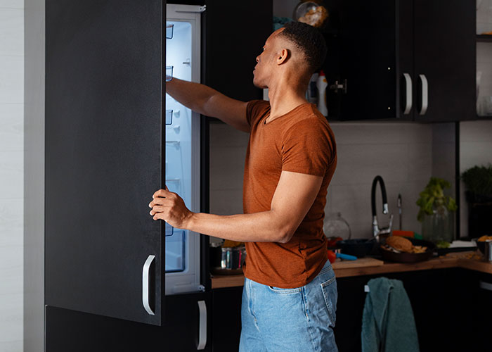 Man in casual clothes opening refrigerator door in kitchen, illustrating darkest secrets people willingly admitted anonymously.