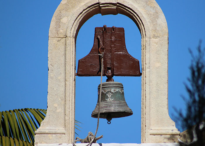 Old bronze bell hanging in a stone arch structure, symbolizing secrets and confessions shared anonymously.