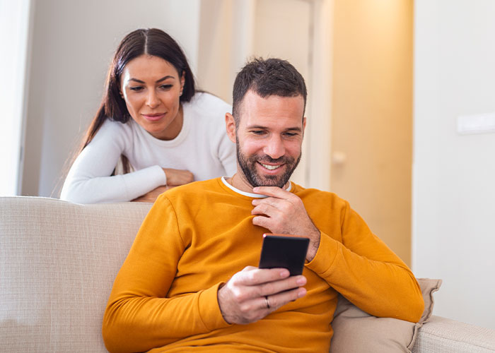 Couple reading anonymous dark secrets on a smartphone, sharing a moment of curiosity and intrigue at home.
