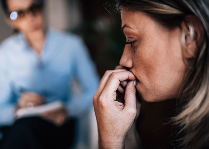 Woman anxiously biting nails during a therapy session, revealing some of the darkest secrets anonymously admitted.