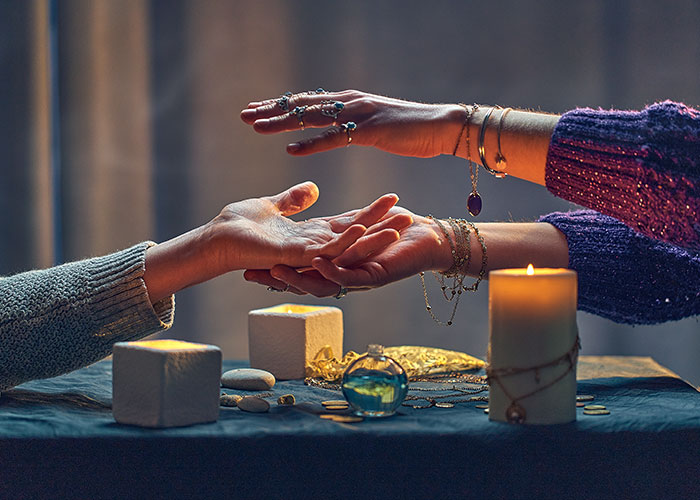 Person reading palm of another with candles and mystical items on table, evoking darkest secrets anonymously shared.