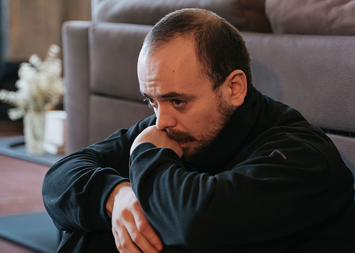 Man sitting on the floor, deep in thought, illustrating emotional impact of darkest secrets people anonymously admitted