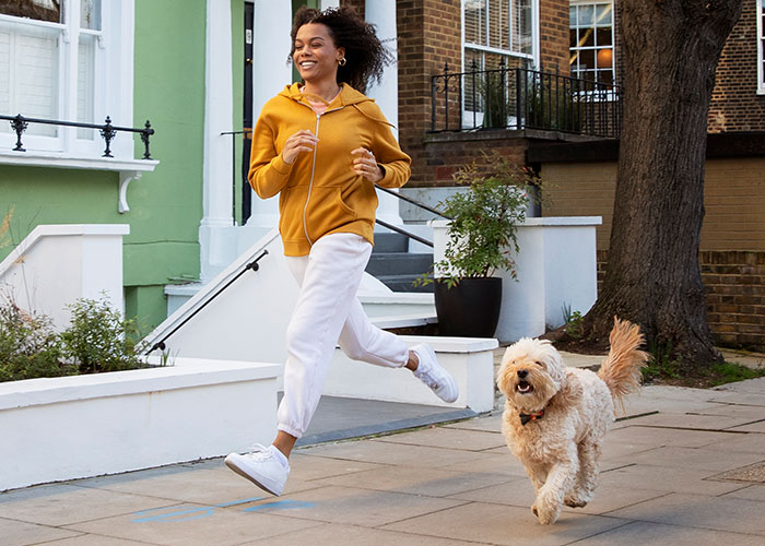 Young woman joyfully running outside with her dog, capturing moments of freedom and happiness in an urban setting.