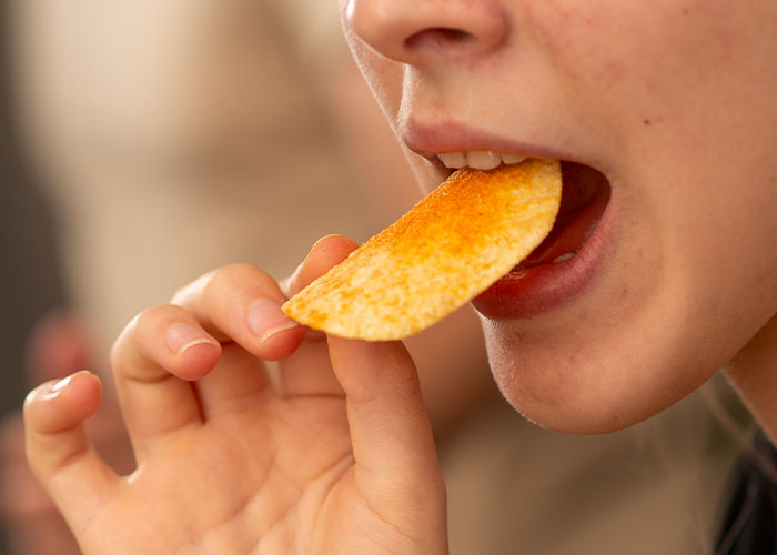 Close-up of a person eating a crispy snack chip, illustrating dark secrets people willingly admitted anonymously.