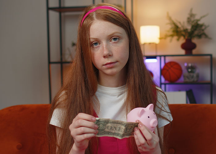 Young girl holding dollar bill and piggy bank, representing anonymous dark secrets about money and personal struggles.