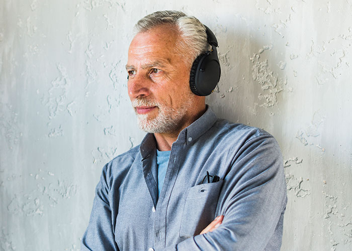 Older man wearing headphones and a blue shirt, listening attentively while reflecting on darkest secrets anonymously.