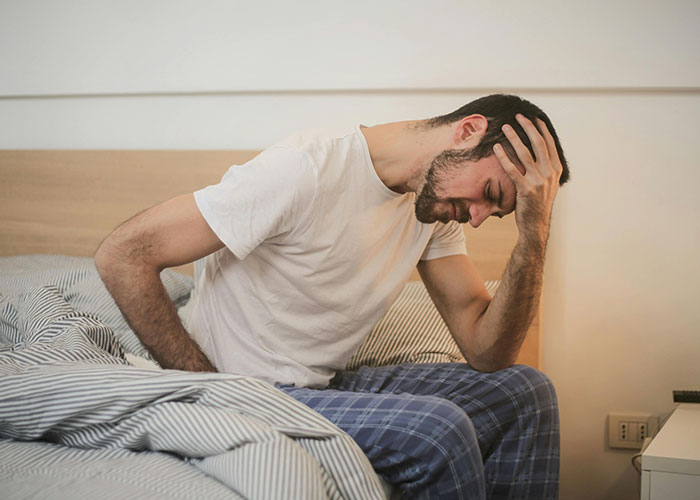 Man in pajamas sitting on bed holding his head in pain, illustrating dark secrets people willingly admitted anonymously.