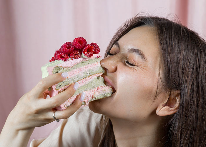 Young woman enjoying a large slice of raspberry cake, capturing a moment of indulgence and dark secrets anonymously shared.