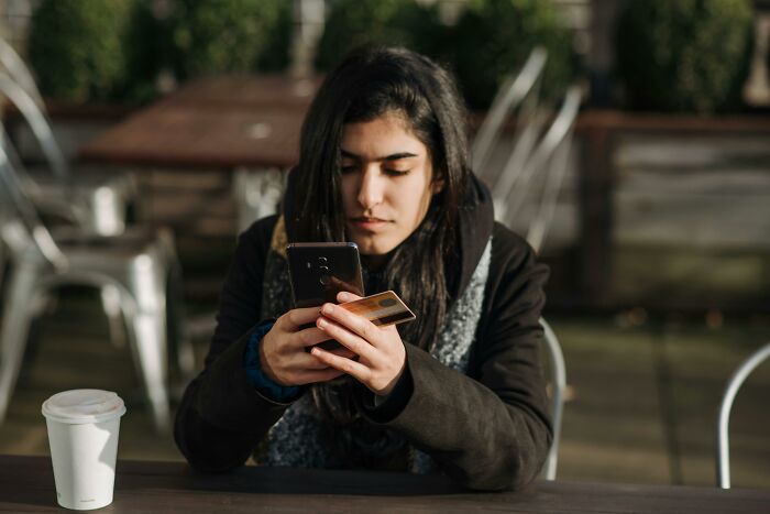 Young woman holding phone and credit card outdoors, reflecting on scary online moments that left her traumatized.