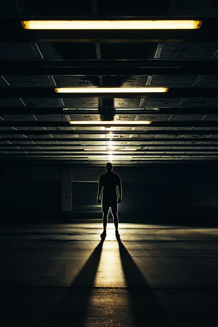 Silhouetted person standing in a dark parking garage with long shadows, evoking scary online moments and trauma.