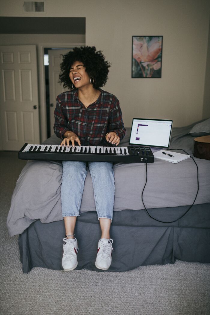 Woman playing keyboard on bed with laptop nearby, representing people sharing scary online moments that left them traumatized.