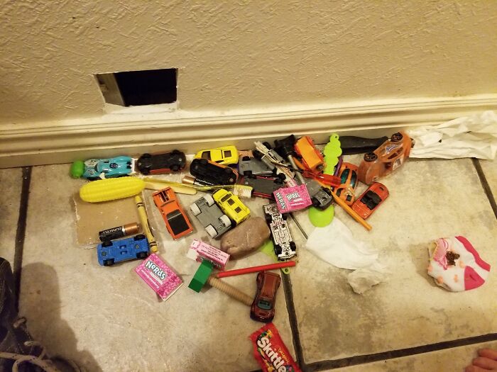 Small toys, candy, and random items found inside a wall opening, illustrating unusual things people found in their walls.