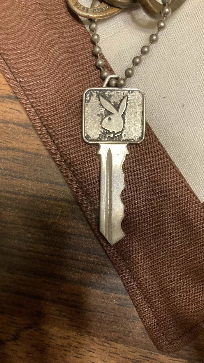 Silver key with a bunny logo on a ball chain resting on a brown fabric, one of the things people found in their walls that confused them