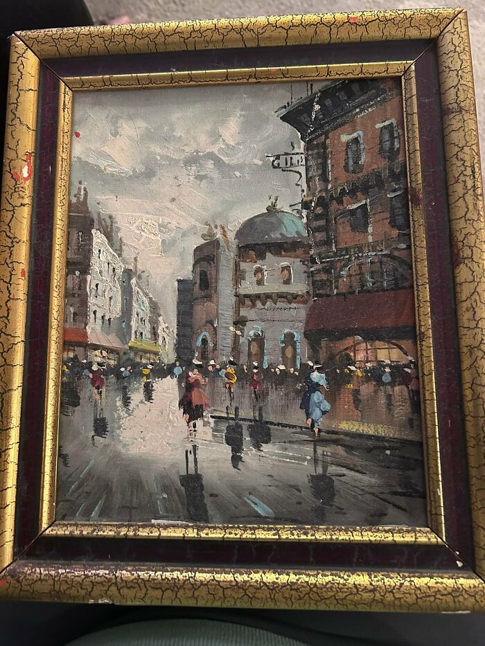 Vintage framed painting found inside a wall depicting a rainy city street scene with people walking and old buildings.