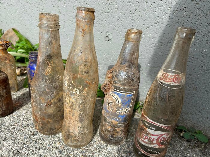 Old rusty vintage soda bottles found in walls and other places, covered in dirt and weathered with age.