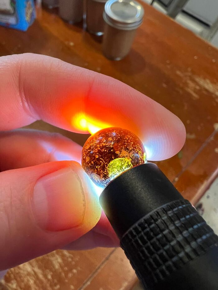 Close-up of a person holding a glowing, translucent amber-like object found in their walls, sparking curiosity and confusion.