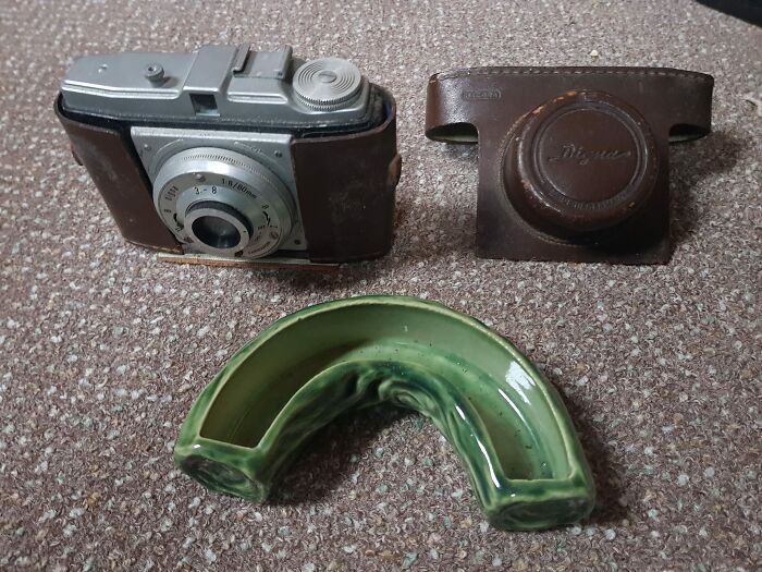 Vintage camera with leather case and a green ceramic object, one of the unusual things people found in their walls or other places.