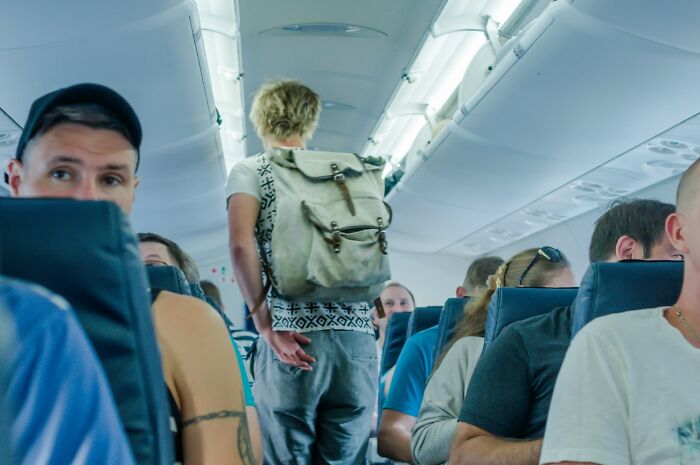 Passengers seated and a traveler walking down the aisle in a packed airplane cabin during a flight trip.