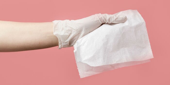 Hand wearing a white glove holding a crumpled white tissue against a pink background related to coworker diabolical things.