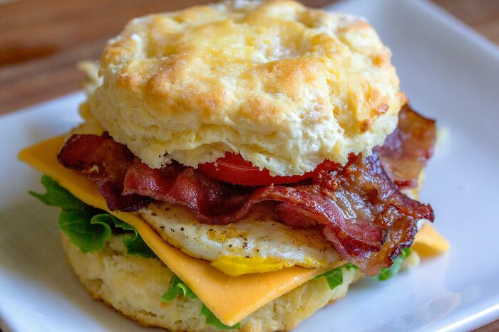 Breakfast biscuit sandwich with bacon, egg, cheese, and lettuce illustrating Americans reveal food habits like breaking spaghetti.