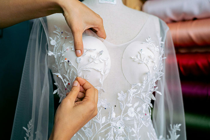 Hands adjusting embroidery on a white wedding dress, highlighting intricate floral details for wedding dress sisters drama.