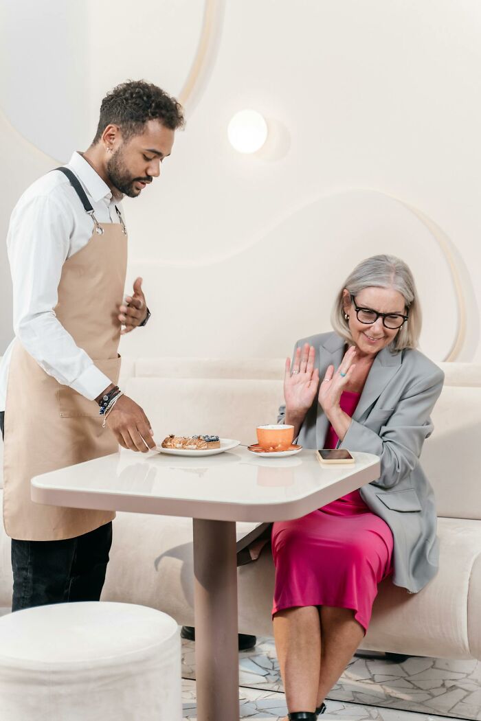 Private resort worker serving food to a seated woman in a modern cafe setting during an ask me anything session.