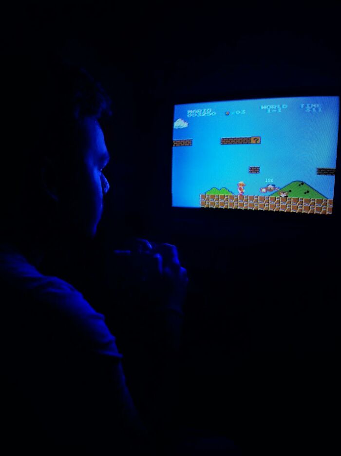 Person playing retro video game in dark room, evoking childhood joys not recorded before smartphones era.