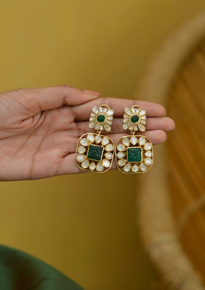 Hand holding intricate earrings with green and white stones, symbolizing women's boldness in relationships and exes.