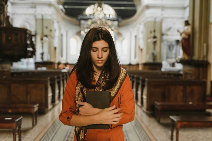 Young woman in an orange dress holding a book, appearing thoughtful and reflecting subtle signs of low self-esteem indoors.
