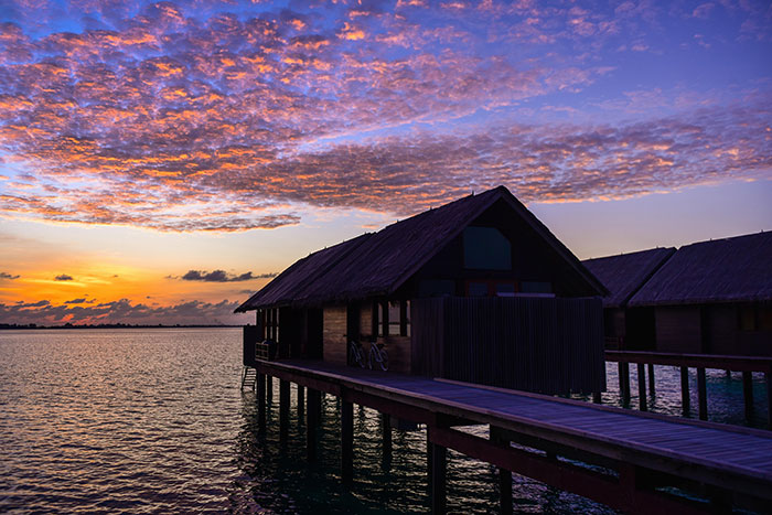 Sunset view of a wooden cabin on stilts over water, illustrating a serene lakeside rental setting.