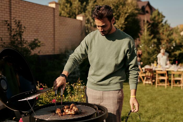 Man grilling chicken outdoors in casual wear.