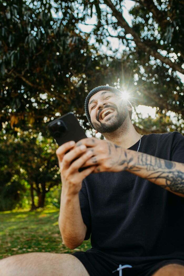 Man with tattoos laughing while holding phone outdoors, capturing best I was there when it was written moments.