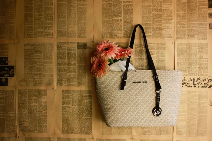 Beige Michael Kors handbag with pink flowers inside, hanging against a vintage newspaper backdrop middle class flag.