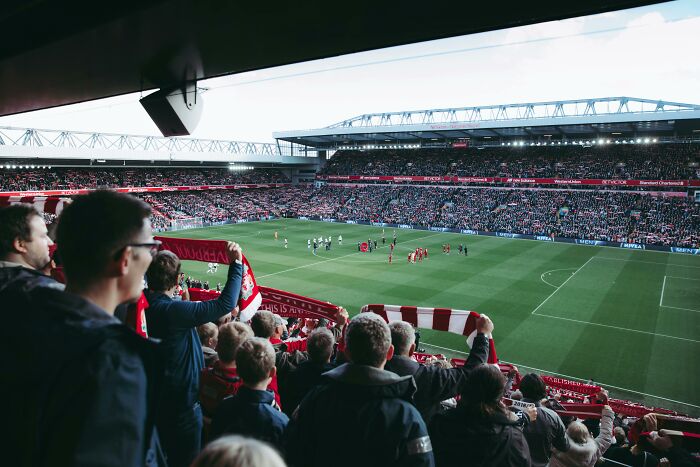 Crowd of fans at a packed UK football stadium, cheering and holding scarves while watching the game on the field.