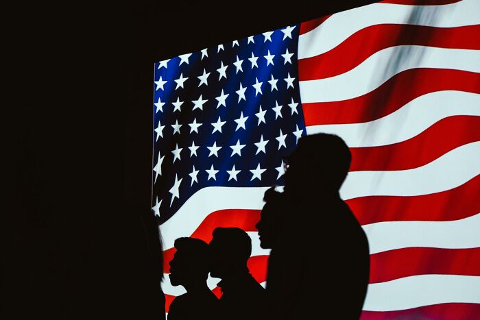 Silhouettes of Americans in front of a large waving flag, symbolizing citizenship and national pride.
