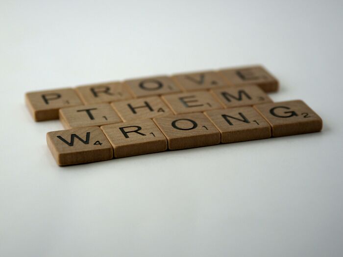 Wooden Scrabble tiles arranged to spell prove them wrong, illustrating a rebus puzzle challenge for smart thinkers.