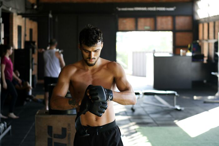 Shirtless man in a gym putting on black gloves, symbolizing strength and determination in personal life challenges.