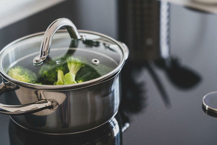 Stainless steel pot with glass lid gently steaming fresh broccoli on a modern stovetop, showcasing tiny gestures in cooking.