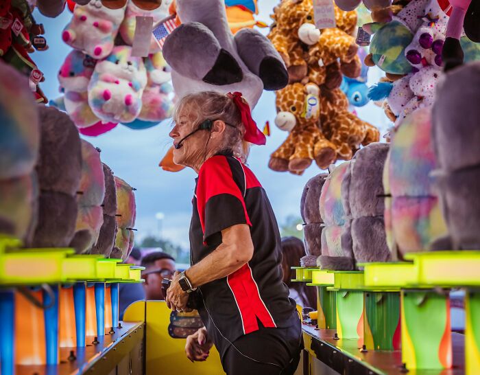Woman in headset working at a carnival game booth surrounded by stuffed animal prizes, highlighting professions attracting awful people - 27