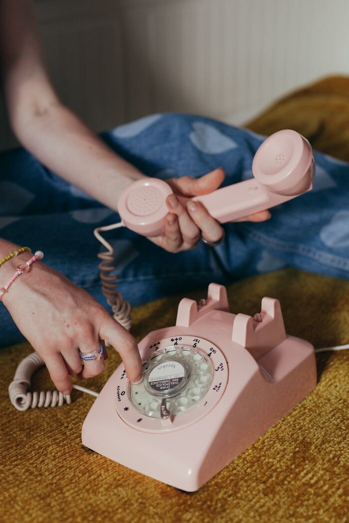 Person using a pink rotary phone, capturing a moment of unique childhood joys before smartphones changed communication.