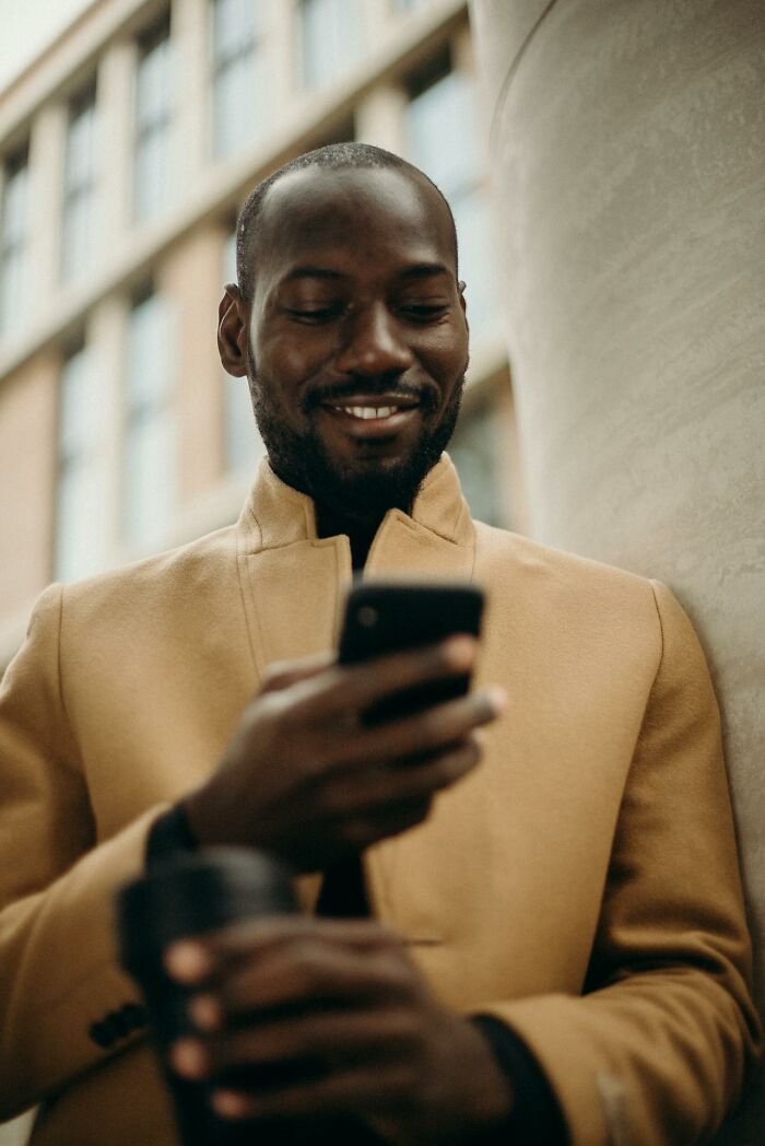 Smiling man holding a phone and coffee cup, standing outdoors while reading messages about wildest things exes got away with.