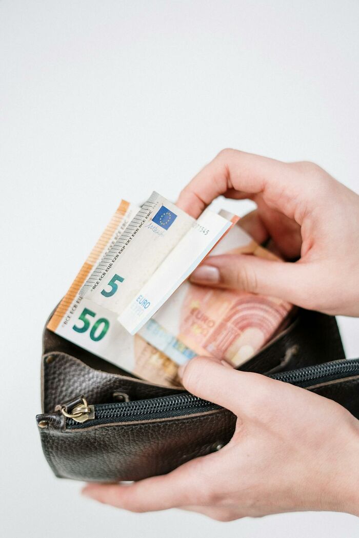 Person holding euros and placing them in a black leather wallet representing private resort worker finances
