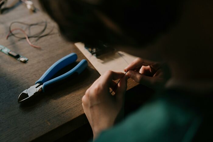 Person making tiny gestures of hands while crafting with small tools on wooden table, charming moment captured.