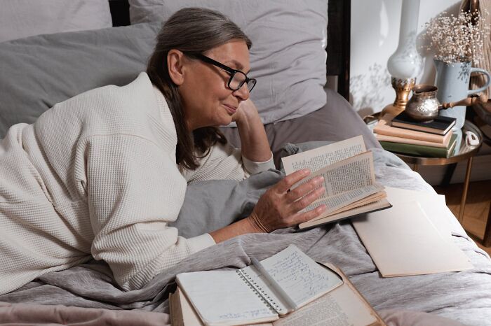 Woman over 42 reading a book in bed, surrounded by notebooks and papers, reflecting on what she won’t tolerate.