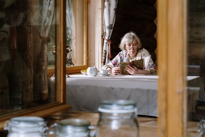 Older woman over 42 reading a book by the window in a cozy wooden home, symbolizing women over 42 mindset shift.
