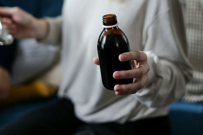 Person in a white sweater holding a dark brown bottle, symbolizing coworker diabolical things to report to HR.