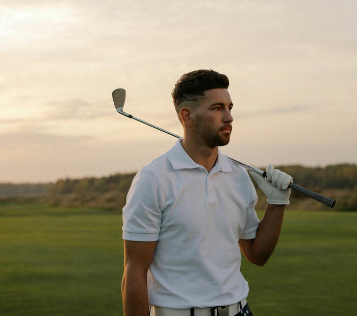 Man in white polo shirt and golf glove holding golf club over shoulder on a private resort golf course at sunset